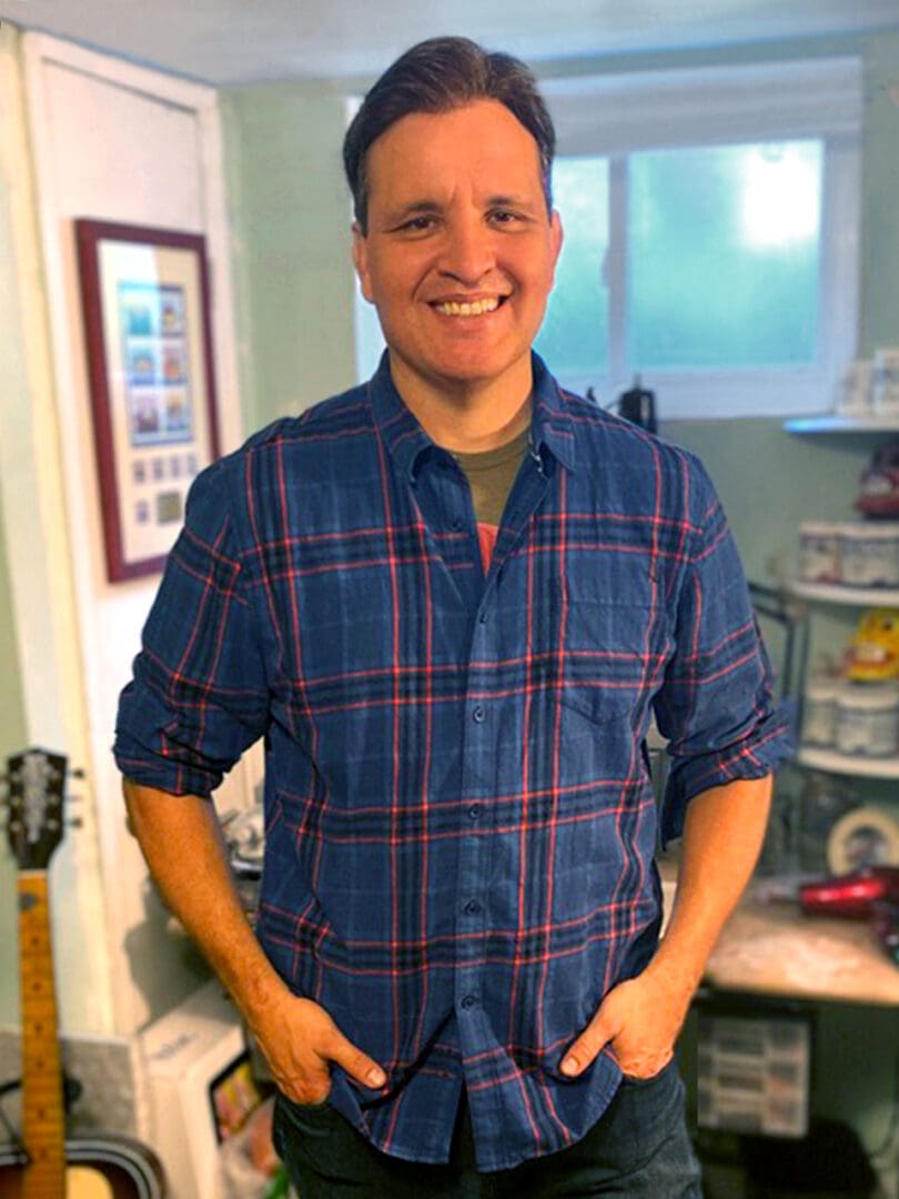 A man in blue shirt standing next to a guitar.