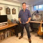 A man standing in front of a desk with a guitar.